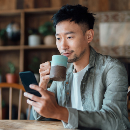 Man sipping from a mug and holding a smartphone